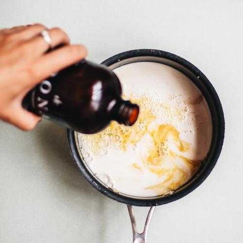 lifestyle photo of person pouring dona unsweetened chai concentrate into a pot with milk